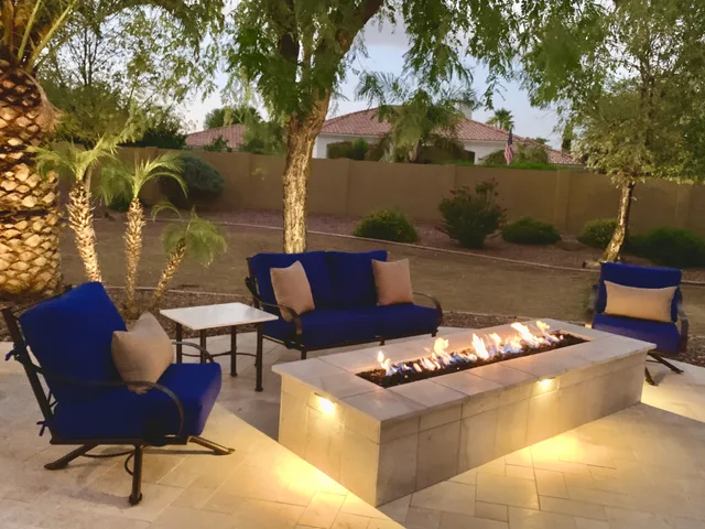 Custom fire features: Linear fire pit at dusk with blue seating on travertine pavers
